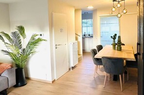 A modern kitchen with a dining area, a potted plant, and a view through the window.