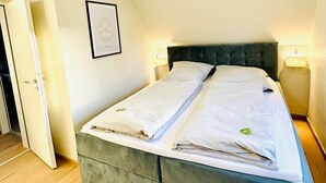 Een tweepersoonsbed met een donker hoofdeinde, twee bedlampjes en een ingelijst schilderij aan de muur.
