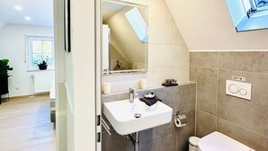 Een moderne badkamer met een wit wastafelmeubel, toilet en douchehoek.