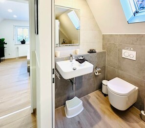 A modern bathroom with a white sink, toilet, and shower area.