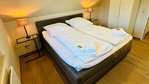 Habitación de hotel con una cama grande, lámparas de noche, armario y suelo de madera.