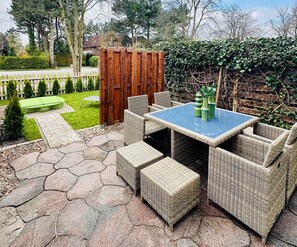 An outdoor patio area with a table and chairs, surrounded by a wooden fence and greenery.