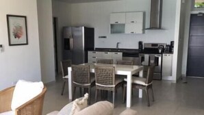 A modern living room with a beige sofa, a dining table with chairs, and a kitchen area in the background. - Luxury Suite 2.4 in Seneca, Point Blanche, St Maarten (Point Blanche)