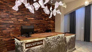 Ein Empfangsschalter mit einem Schild, das 'RECEPTION' zeigt, eine Holzwand mit Fischgrätmuster und hängende Papierlampen.