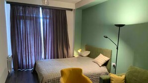Een hotelkamer met een bed, een groene bank, een gele fauteuil en een vloerlamp.