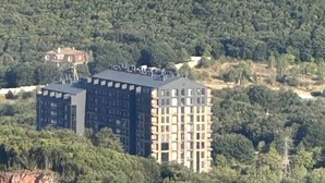 Een meerhoog gebouw met een plat dak, omringd door weelderige begroeiing en heuvels.