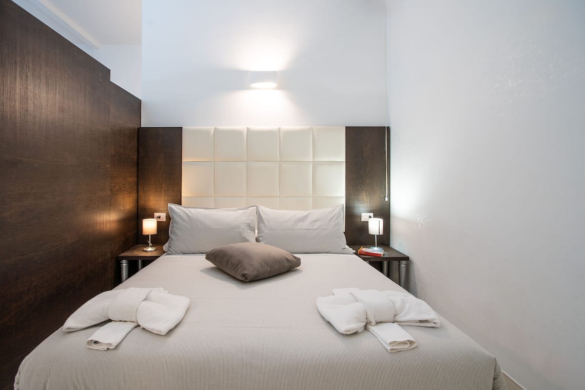Ein Hotelzimmer mit einem großen Bett, zwei Nachttischen mit Lampen, einer Kopfteil mit einer Lichtleiste und ordentlich gefalteten Handtüchern auf dem Bett.
