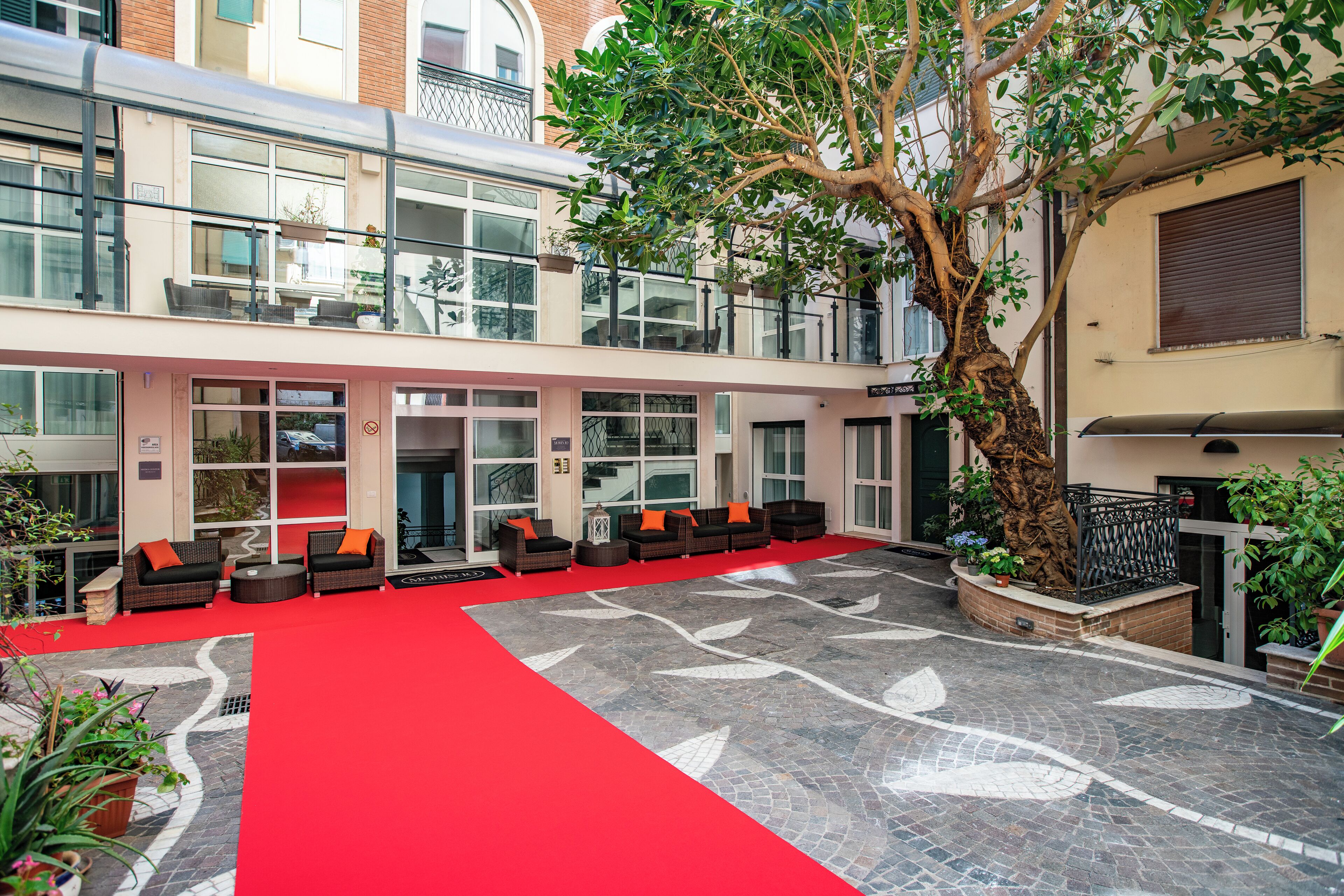 Un hall de hotel con alfombra roja, zona de estar al aire libre y un gran árbol.