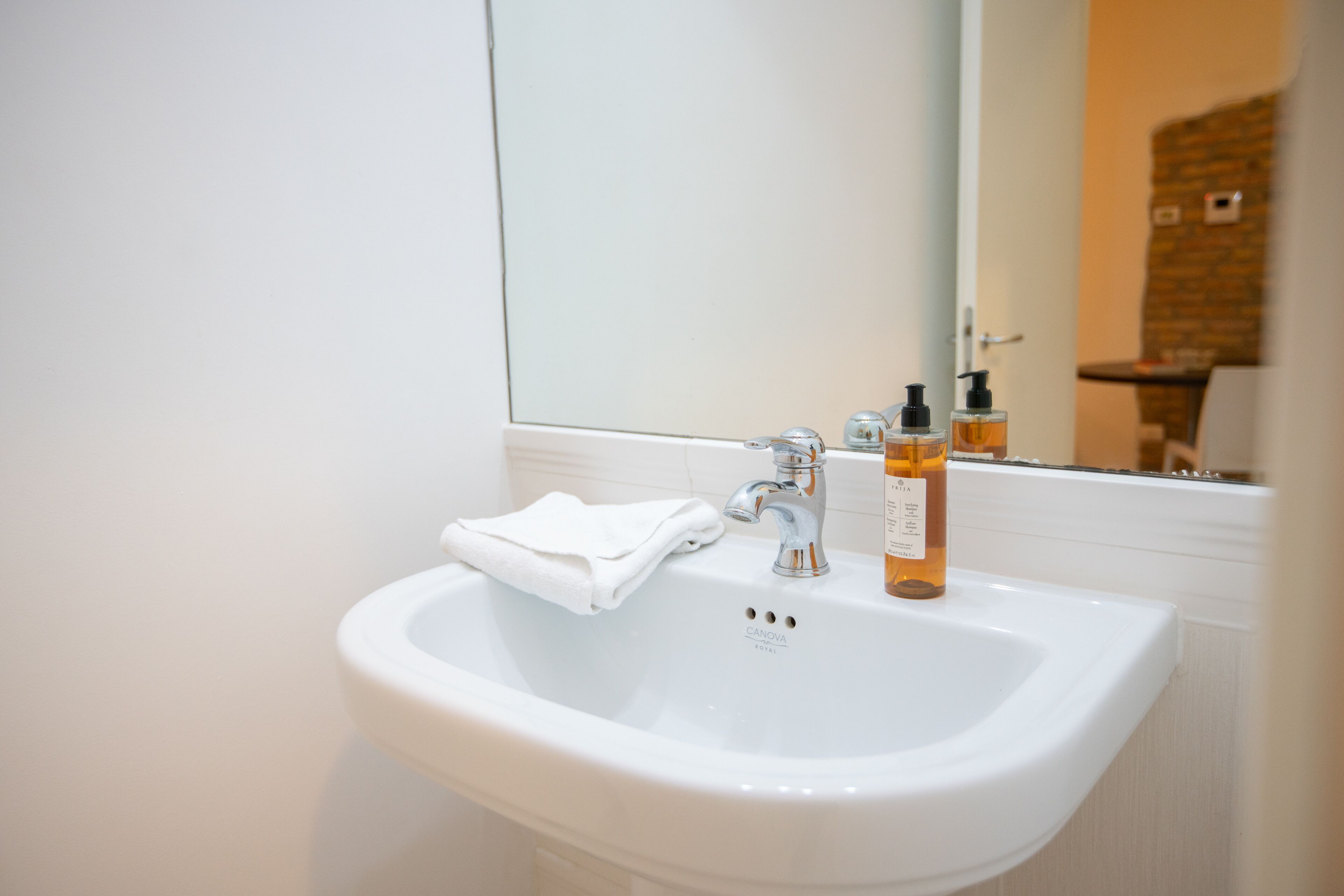 A white bathroom sink with a mirror above it, a towel hanging on the side, and two bottles of lotion on the sink.