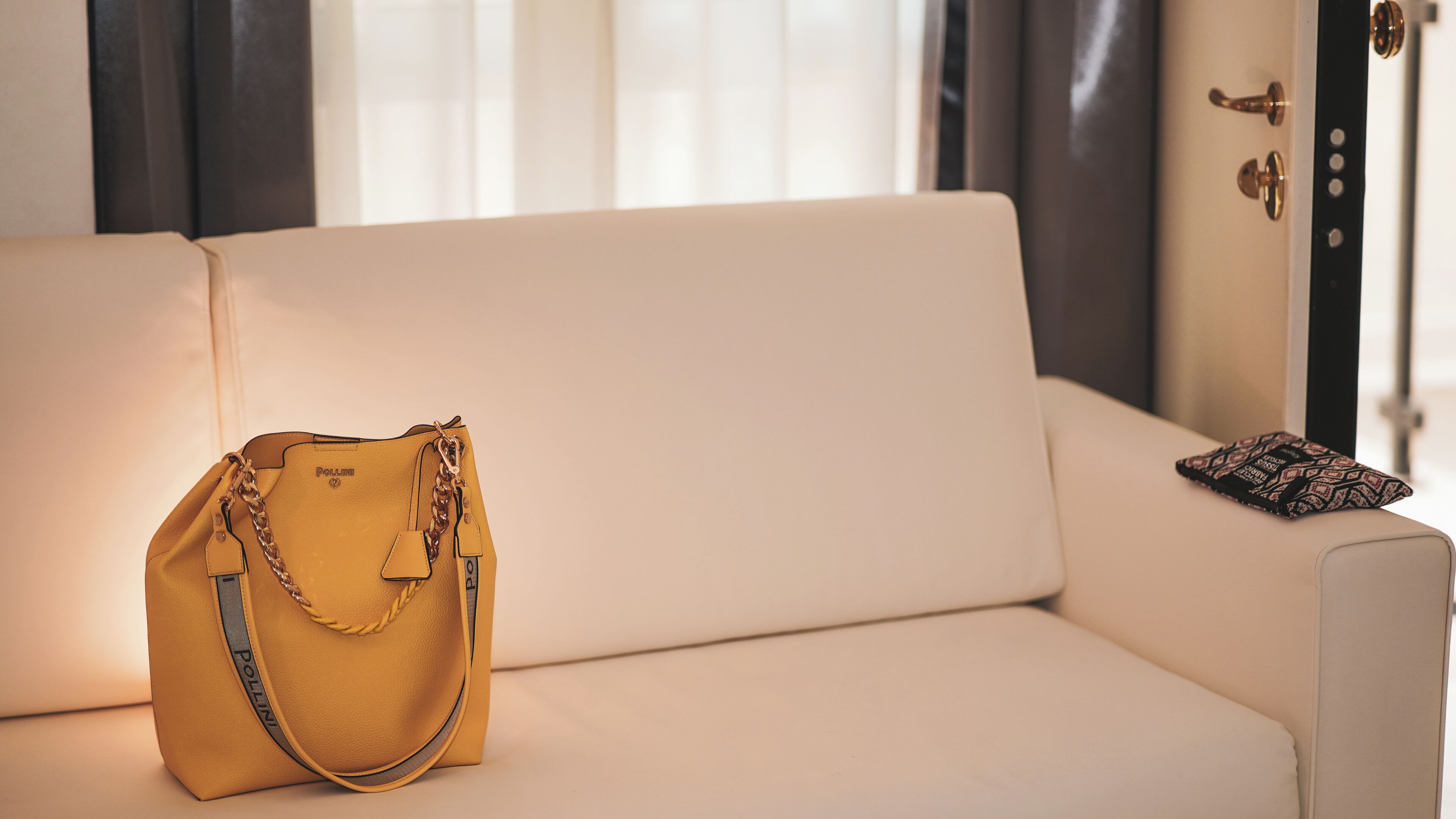 A beige sofa with a yellow handbag and a patterned pillow.