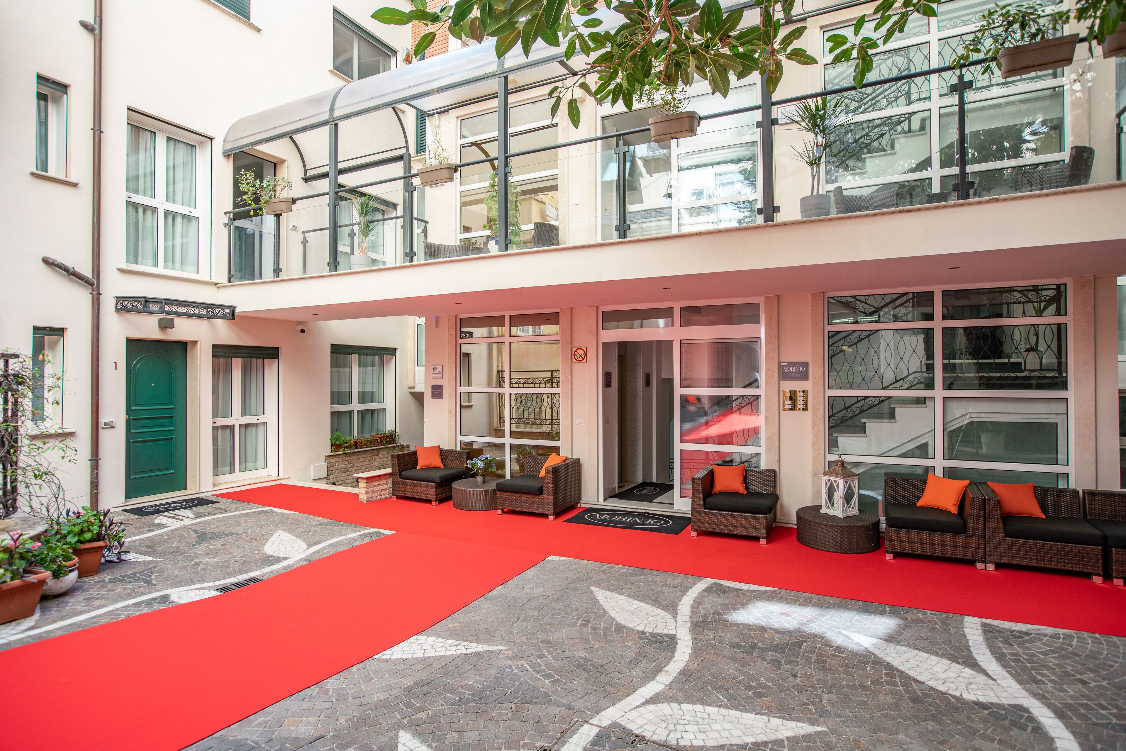 A hotel lobby with a red carpet, wicker sofas with orange cushions, and potted plants.