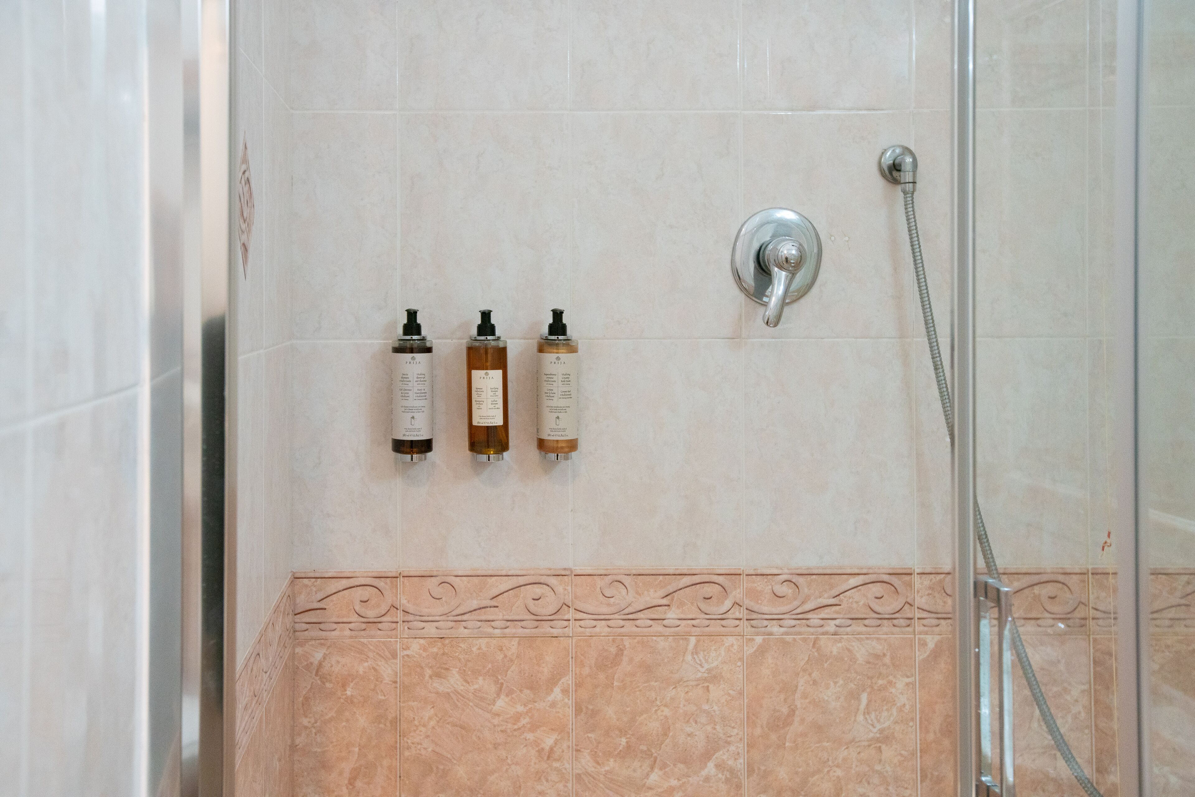 Et bruseområde med glasdør, armatur på væggen og tre shampoo-flasker.