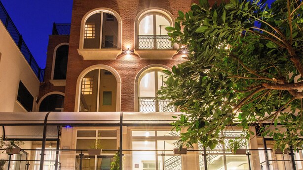 A multi-story hotel with a red carpet entrance, outdoor seating area, and a balcony with a railing.