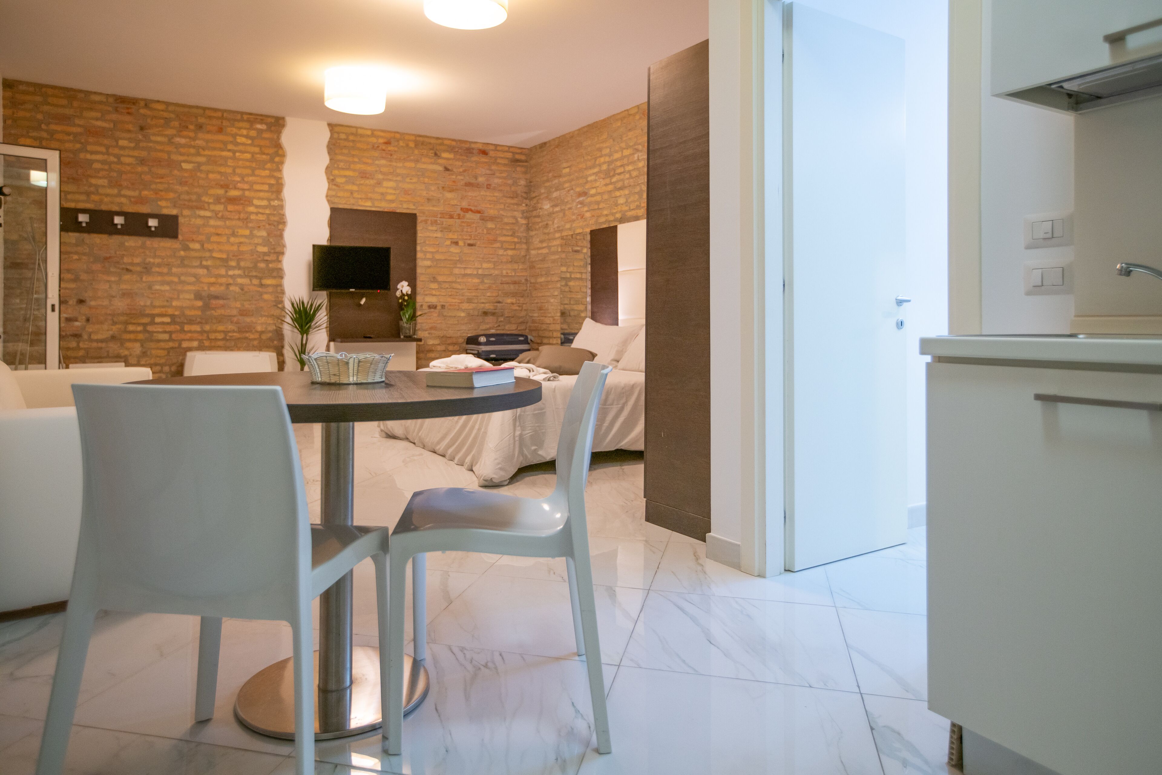 A modern room with a brick wall, a dining area with a table and chairs, a sofa, and a TV mounted on the wall.