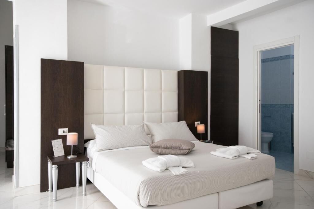 A modern hotel room with a large bed, a bedside table with a lamp, and a view of the bathroom.