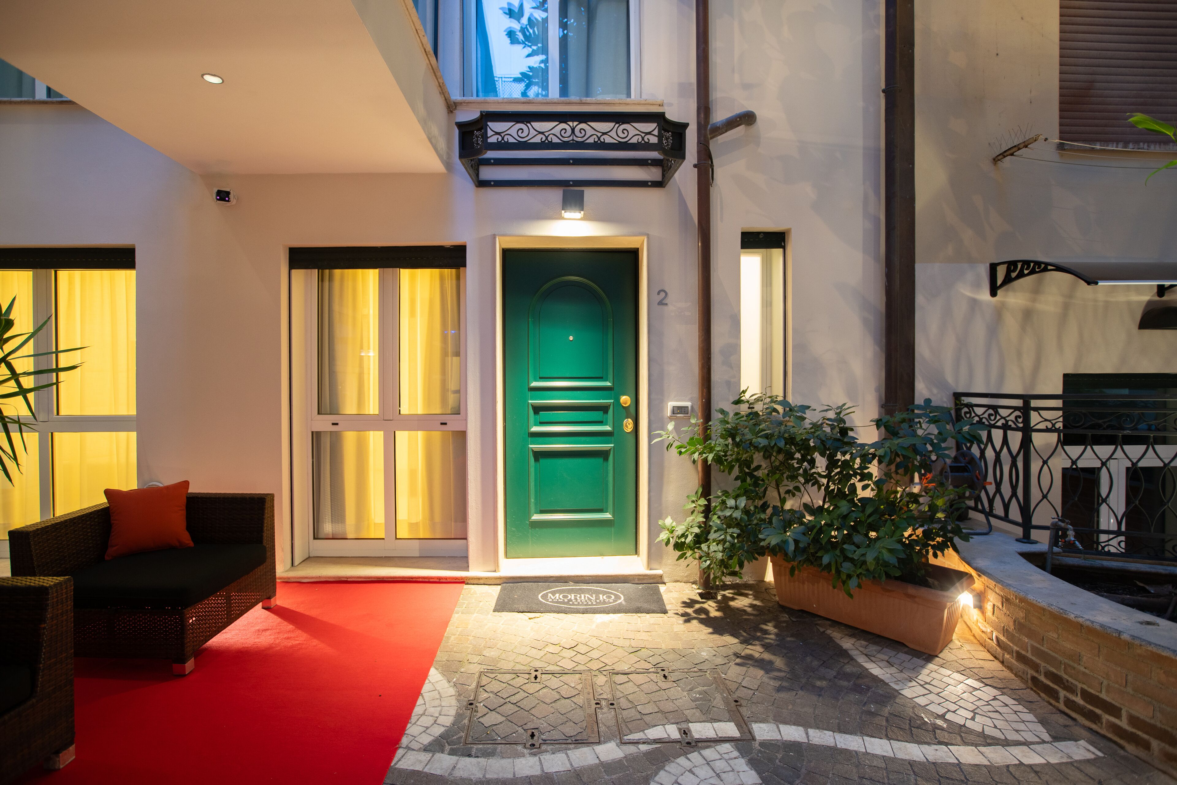A modern building entrance with a green door, a red carpet, and a potted plant.