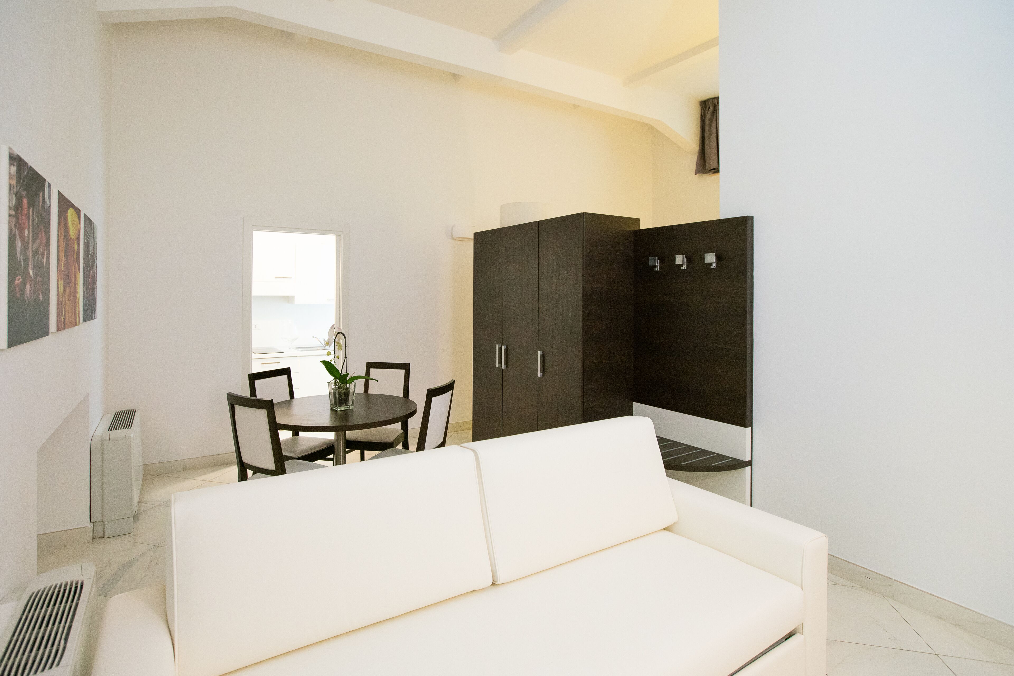 A modern living room with a white sofa, a dining table with chairs, and a dark cabinet.
