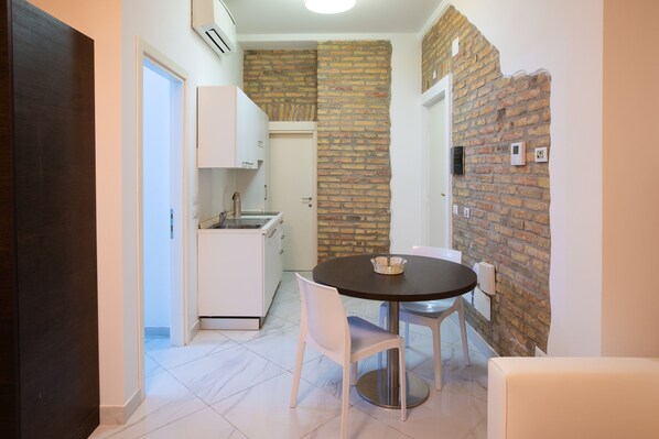 Una cocina compacta con armarios blancos, encimera negra y una pared decorativa de ladrillo.