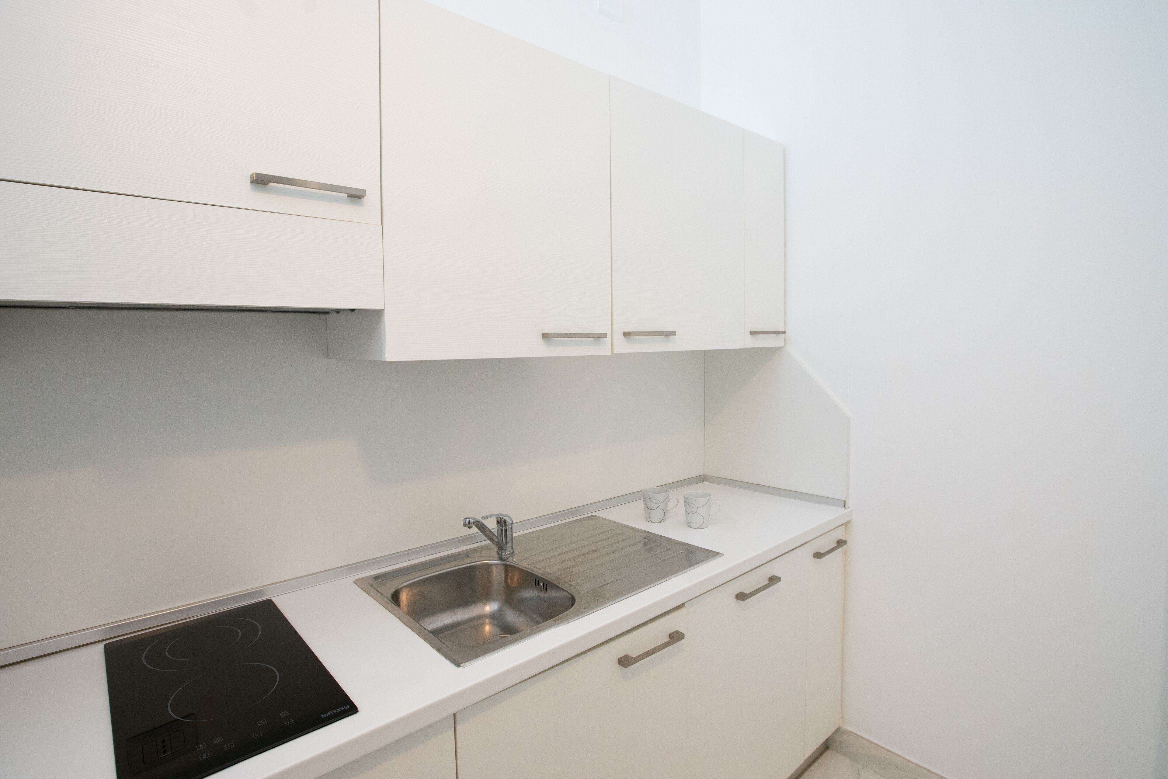 Una cucina moderna con mobili bianchi, un lavello in acciaio inossidabile e un piano cottura a induzione nero.
