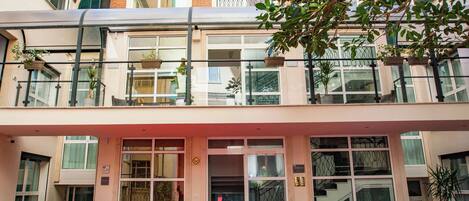 Um hotel com entrada de tapete vermelho, área externa com sofás e fachada de tijolos.
