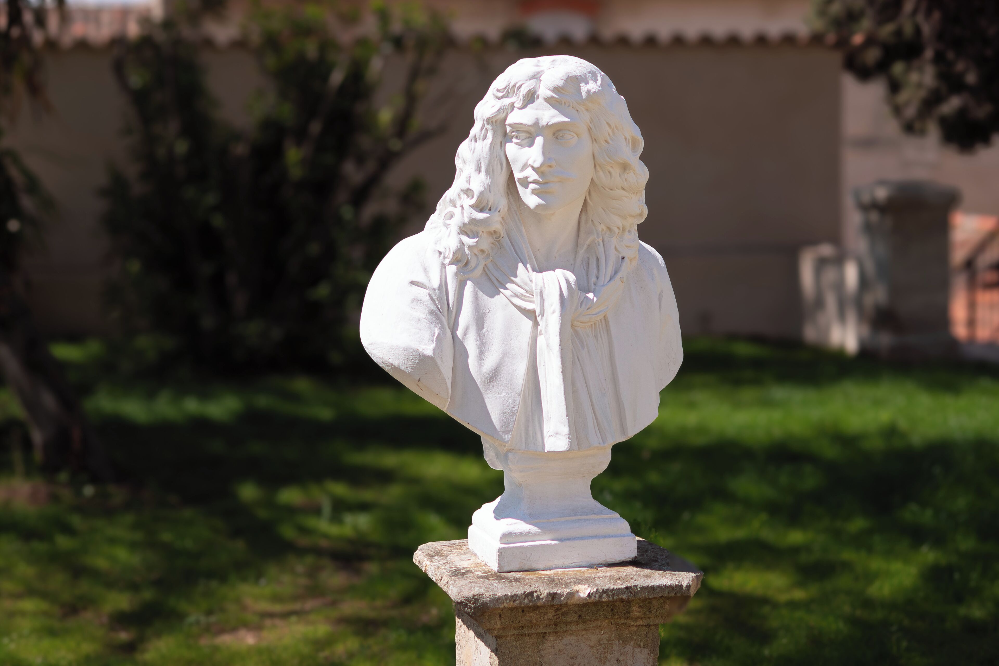 Una escultura de busto blanco sobre un pedestal de piedra en un jardín.