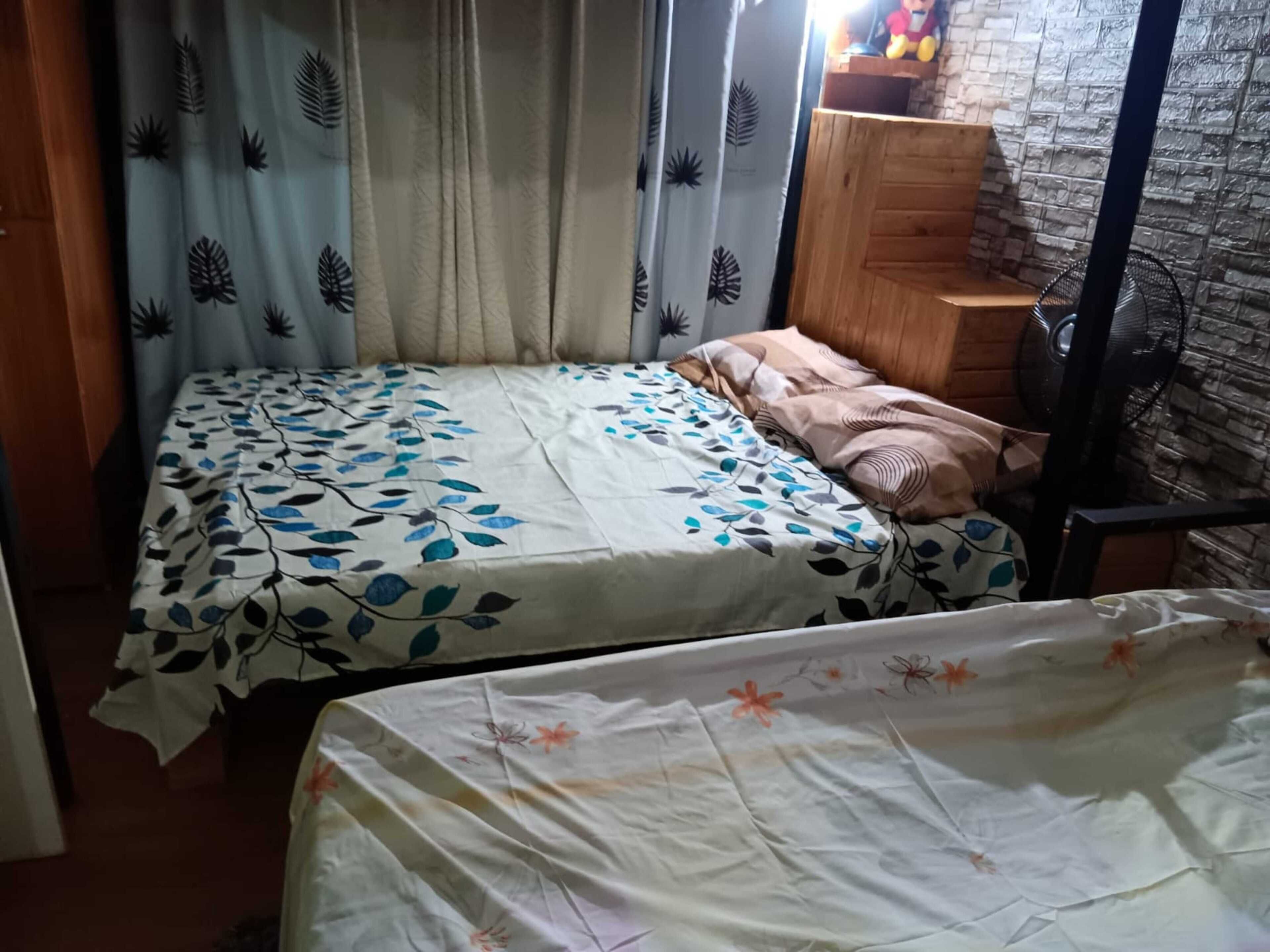 A bedroom with two beds, a wooden headboard, a fan, and a brick wall.