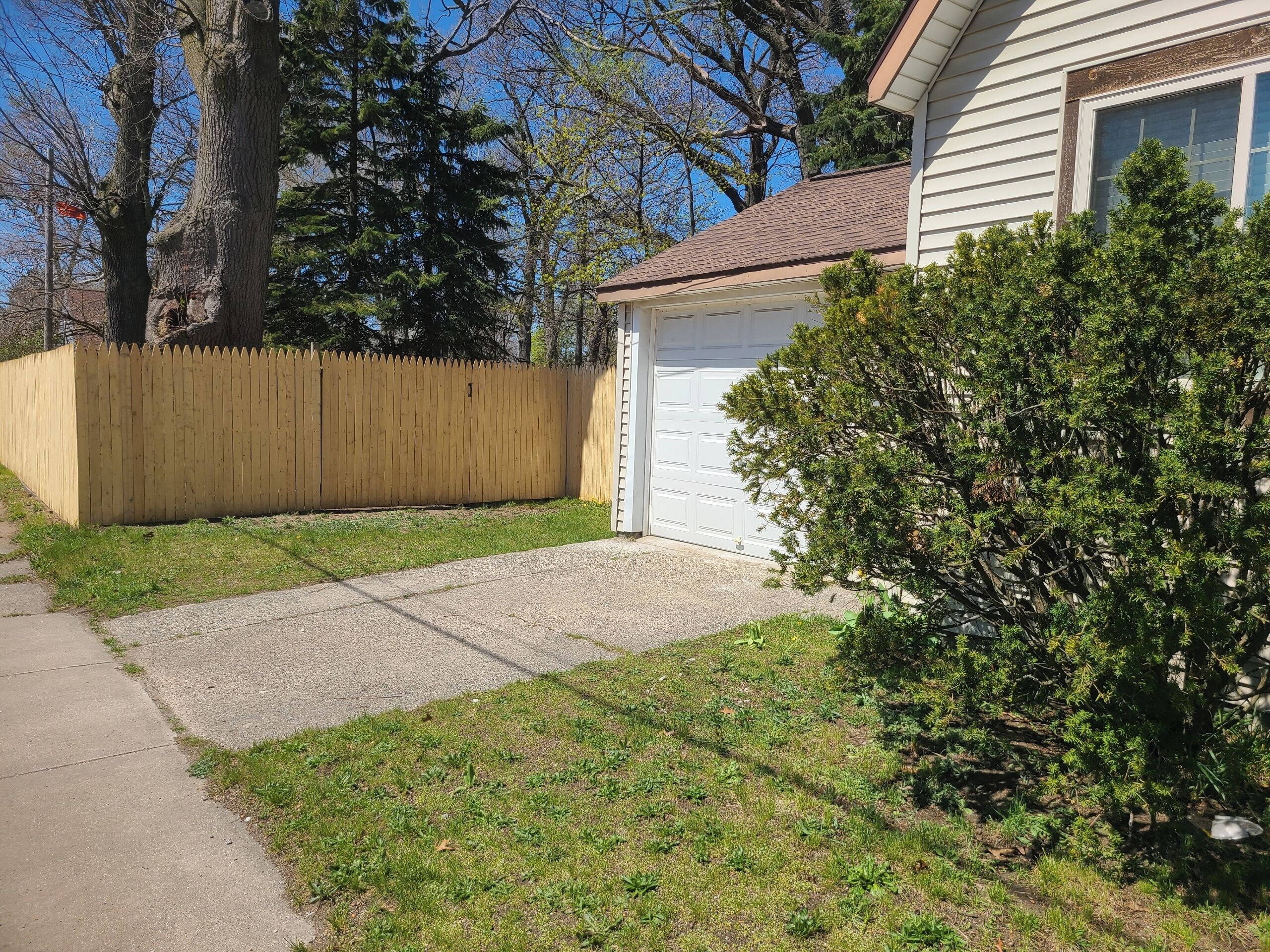 A residential driveway with a wooden fence, a garage, and a well-maintained lawn.