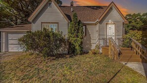 A two-story house with a garage, a front porch, and a staircase leading to the entrance. - Cozy 2 Bedroom with King Bed, 2 Full Bathrooms Conveniently located in the heart of Muskegon!!! (Muskegon)
