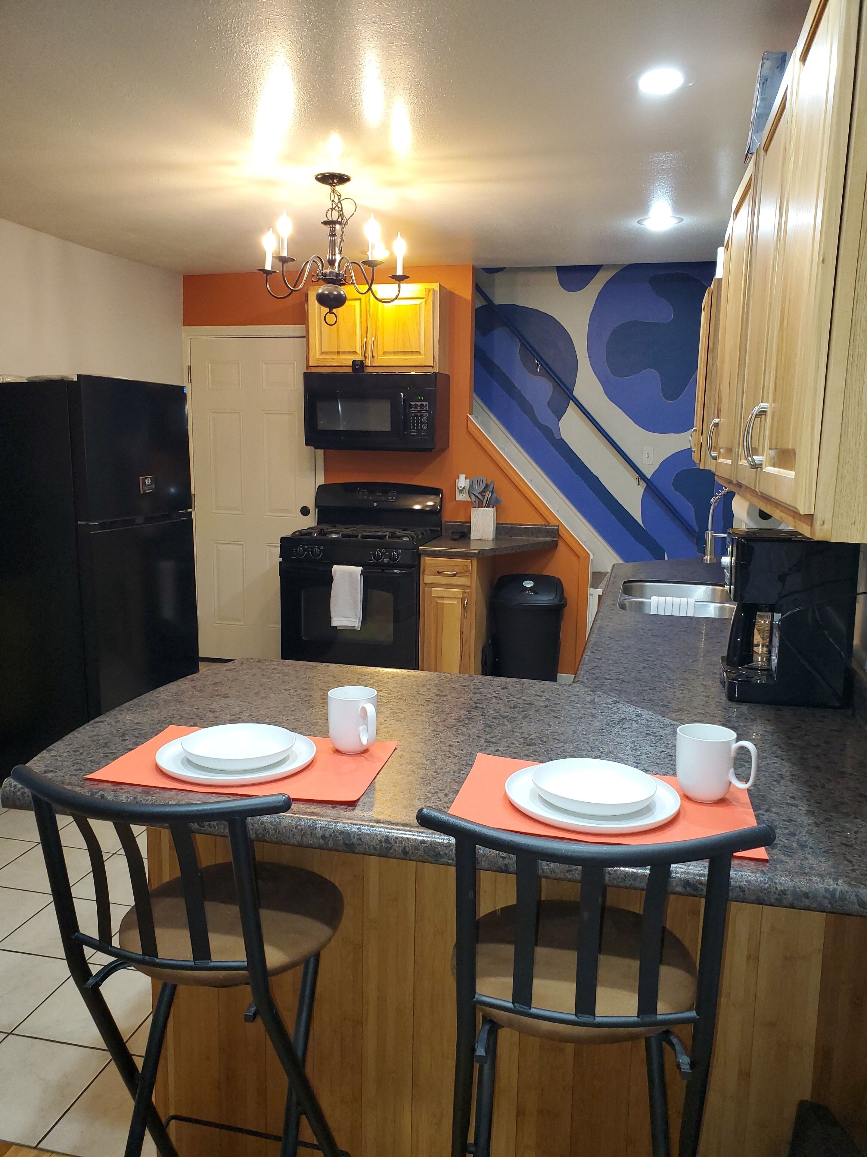 Une cuisine dotée d’un îlot central, de deux tabourets de bar, d’un réfrigérateur, d’une cuisinière, d’un four à micro-ondes et d’un évier.