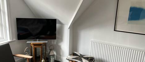 A modern living room with a flat-screen TV, a grey sofa, a wooden coffee table, and a unique patterned stool.