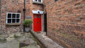 A narrow alleyway with a red door, a small potted plant, and a brick wall.
