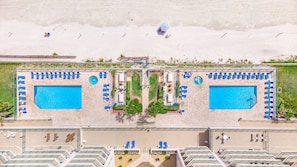 Eine Luftaufnahme eines Resorts mit zwei Swimmingpools, Liegestühlen und einem Strandabschnitt.