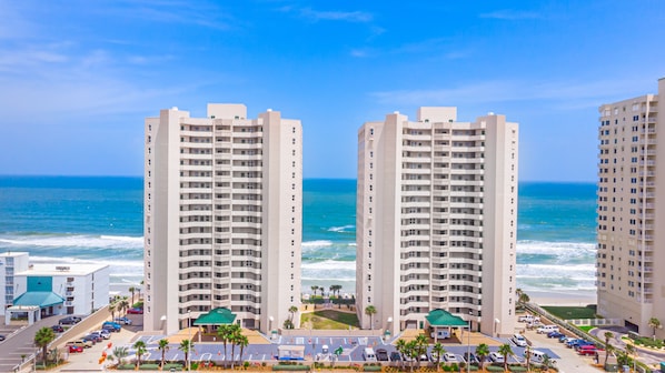 A high-rise hotel with multiple floors, a parking lot, and a view of the ocean. - Oceanfront | Heated Pool-Twin Towers #1406 (Daytona Beach Shores)
