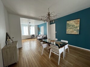Una sala de estar moderna con comedor, que incluye una mesa de vidrio, sillas blancas y una pared azul decorativa.
