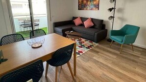 Un saló modern amb un sofà, una butaca color turquesa, una taula de dinar amb caires i una alfombra colorida.