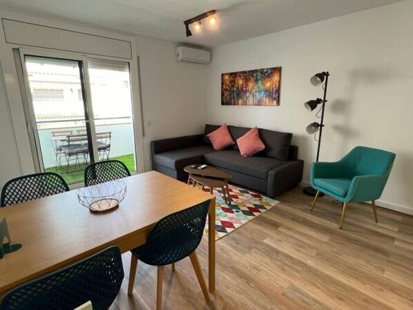 A modern living room with a sofa, a teal armchair, a dining table with chairs, and a colorful rug. - Beautiful refurbished flat in Roses AV-15 (Roses)