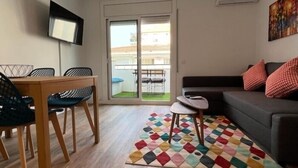 Un saló modern amb zona de menjador, un sofà, una catifa colorida i una porta corredissa de vidre que dona a un balcó.