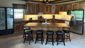 A spacious kitchen with wooden cabinets, a large island with stools, a stainless steel refrigerator, and a stone backsplash. - Nature's Retreat: Ultimate ATV & Fishing Getaway minutes from Cherry Springs (Galeton)