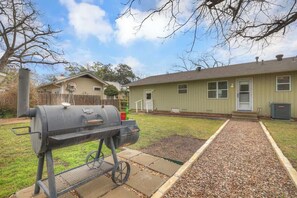 A backyard with a barbecue grill, a pathway, and a house with a green exterior.