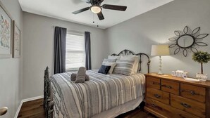 Ein Schlafzimmer mit einem Bett, einer Holzkommode, einem Deckenventilator und einem Wandspiegel.