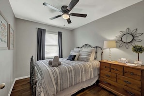 A bedroom with a bed, a ceiling fan, a dresser, and a wall-mounted mirror.