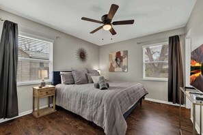 Une chambre à coucher avec un lit, un ventilateur de plafond, une table de chevet, une lampe et un tableau au mur.