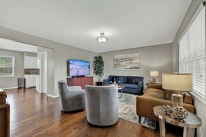 Ein modernes Wohnzimmer mit Flachbildfernseher, grauen Sesseln, einem blauen Sofa und einem Couchtisch.