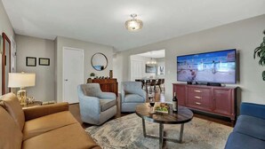 Una sala de estar con un sofá, sillones, una mesa de centro, un televisor y un comedor al fondo.