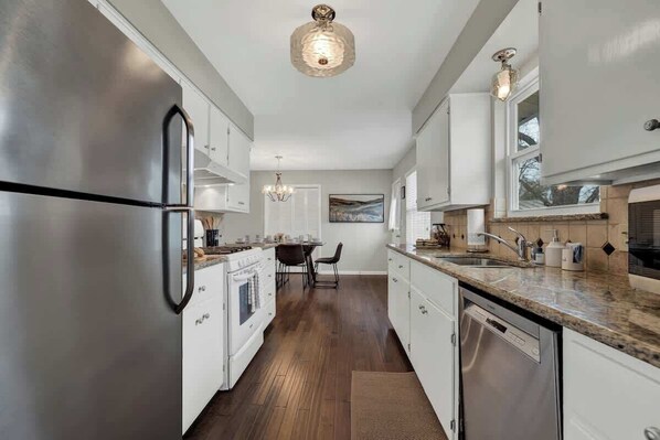 A modern kitchen with stainless steel appliances, white cabinetry, and a granite countertop.