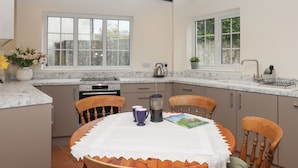 Een moderne keuken met een marmeren aanrecht, houten stoelen en een eettafel met een kanttafelkleed.