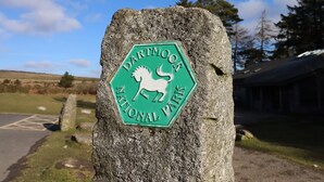 Een stenen paal met een groen bord dat Dartmoor Nationaal Park aanduidt.