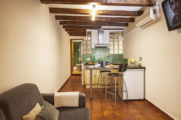 A compact kitchen with a dining area, a small refrigerator, and a TV mounted on the wall. - BeBarceloner Gothic Quarter Studios (Barcelona)