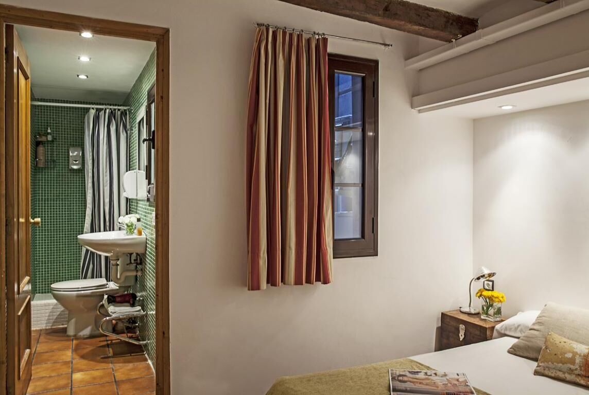 Ein Schlafzimmer mit einem Bett, einem Nachttisch mit Lampe und einem Fenster mit Vorhängen.