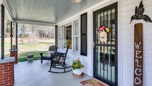 A porch with a rocking chair, a potted plant, and a welcome sign.